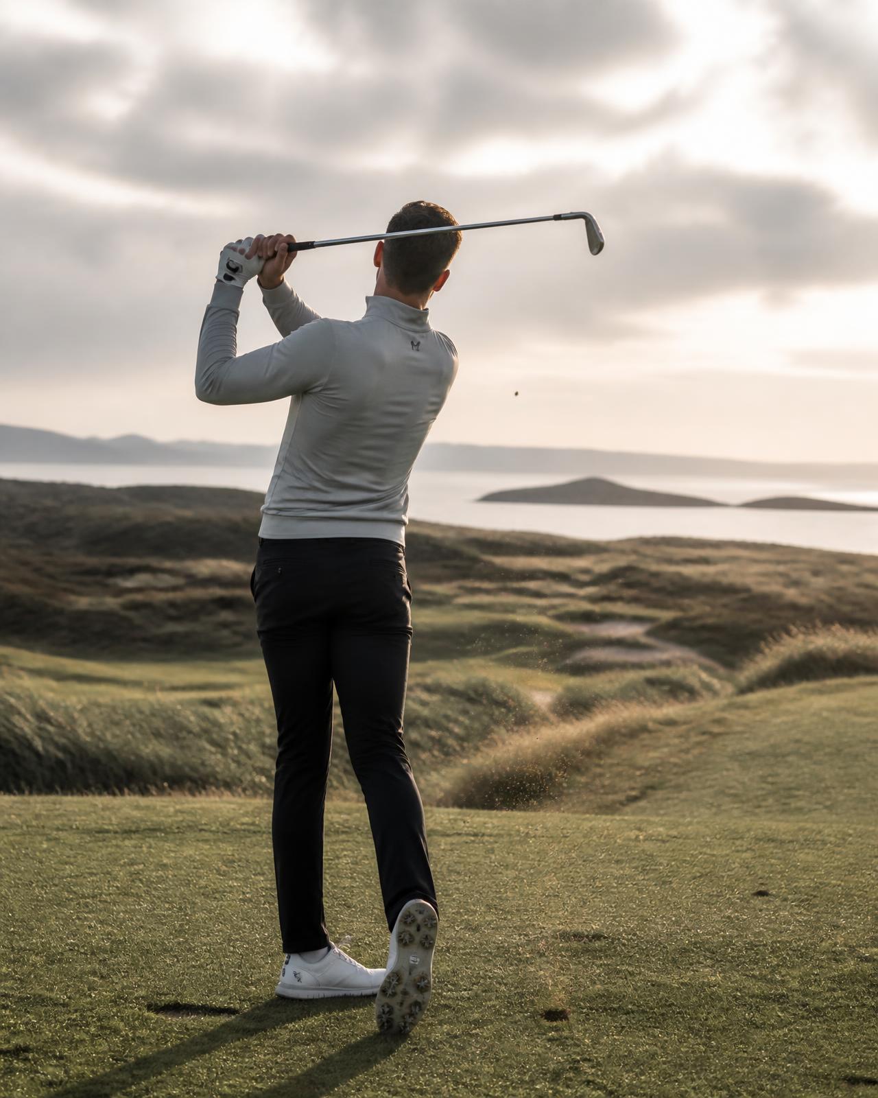 Golfer striking an iron shot on a coastal course